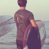 Surfista sulla spiaggia con tavola e t-shirt grigia con stampa Ride or Die Costa Est Beachwear