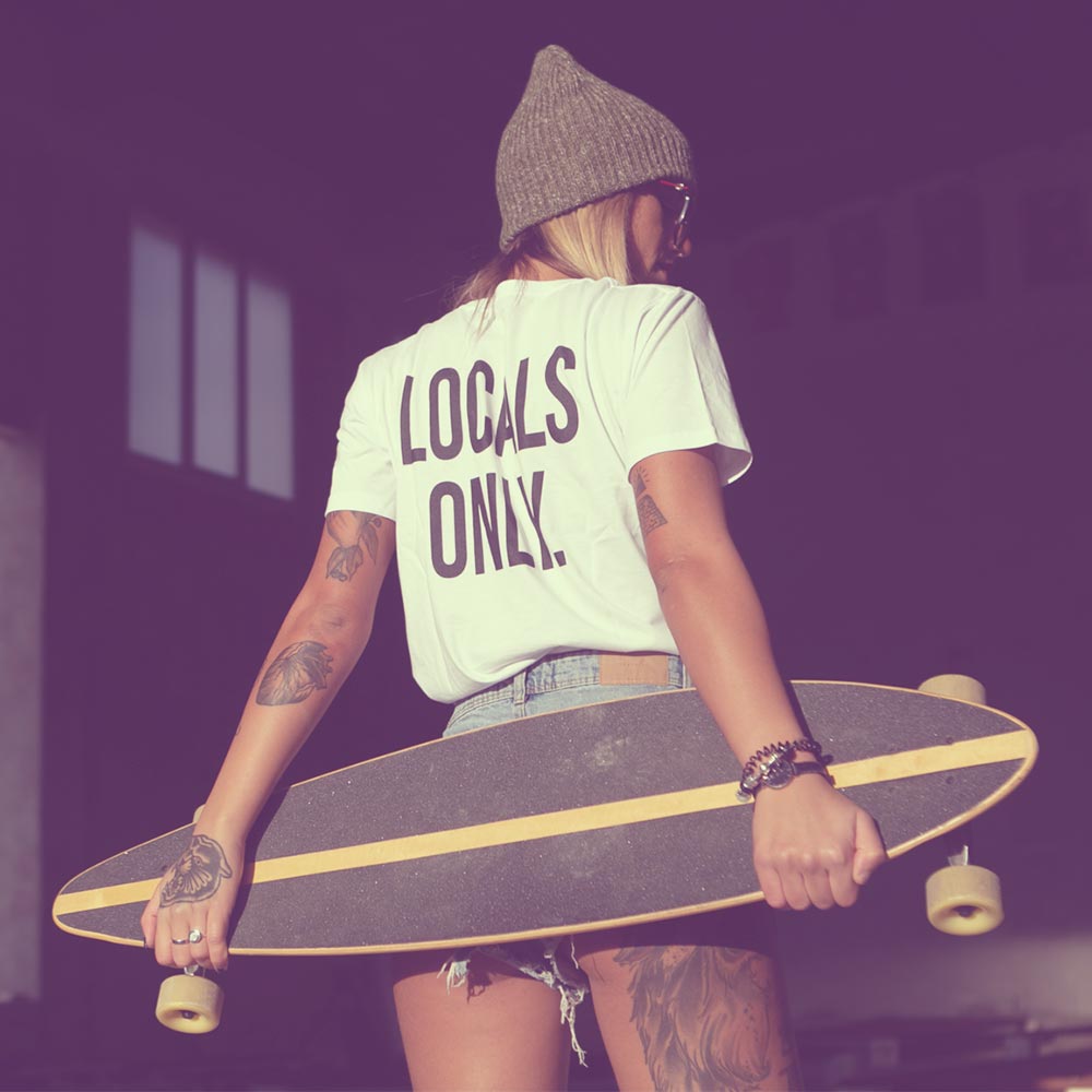 Ragazza con tatuaggi, skate e t-shirt bianca Locals Only di Costa Est Beachwear